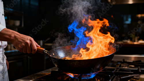 Professional chef flambeing food in wok with dramatic blue and orange fire flames in restaurant kitchen