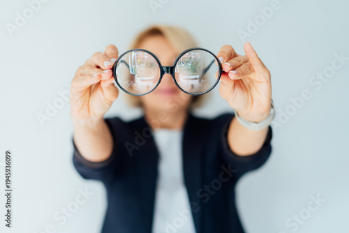 Fotografie Focus on eyeglasses in the hands of blurred businesswoman on isolated white background