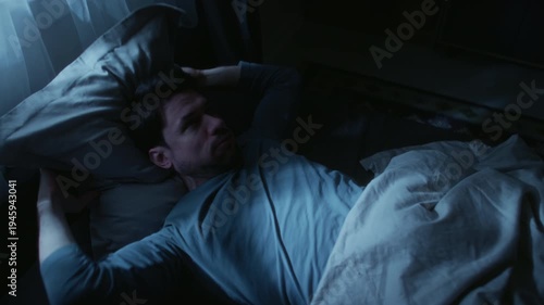 Middle aged man suffering from sleep deprivation feeling discomfort while lying in bed, tossing pillow up to get to sleep at late night