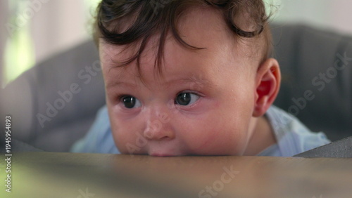 Baby lying on dining table, biting surface, big-eyed expression, early childhood sensory exploration, teething behavior, curious moment of discovery, indoor home setting