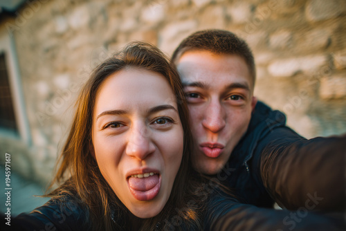Cheerful young couple making funny faces while taking a wide-angle selfie on city street