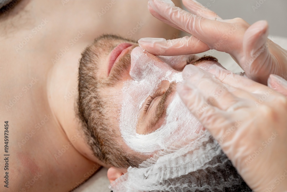 Naklejka premium A cosmetologist cleanses a man's face. The man undergoes facial treatments at a cosmetic clinic. Men's cosmetology