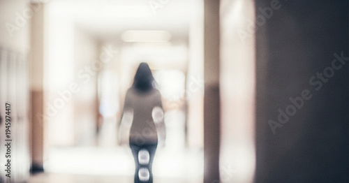 A blurry silhouette of a person walking down a school hallway, with lockers lining the walls. Soft focus highlights the sense of movement and solitude.