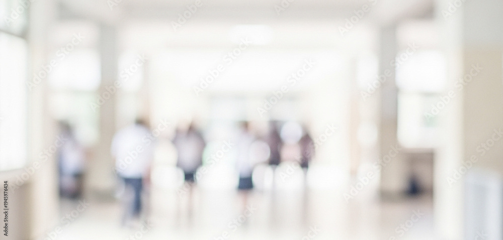 Fototapeta premium A blurred image of people walking in a brightly lit hallway. The soft focus creates a sense of movement and activity in a modern building setting.