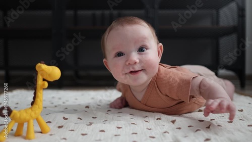 Baby lying on a floor mat next to a giraffe toy, looking at the camera and drooling