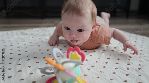 Baby lying on a mat, looking down at a toy with focus and drooling on the blanket