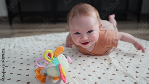 Happy baby on a mat reaching for a colorful toy, smiling and laughing during tummy time.