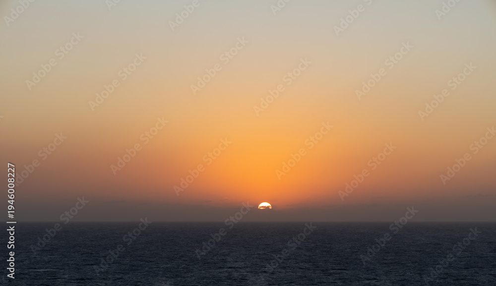 Fototapeta premium Golden sunset over ocean horizon with vibrant orange sky and calm sea