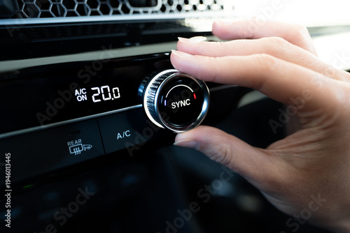 close-up of hand adjusting the dual climate control knob (AC air conditioning) in a modern car dashboard showing twenty degrees celsius on a digital display with sync function