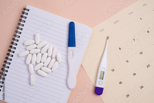 Test stick on monthly calendar and vitamins on spiral notebook. Pregnancy planning concept.