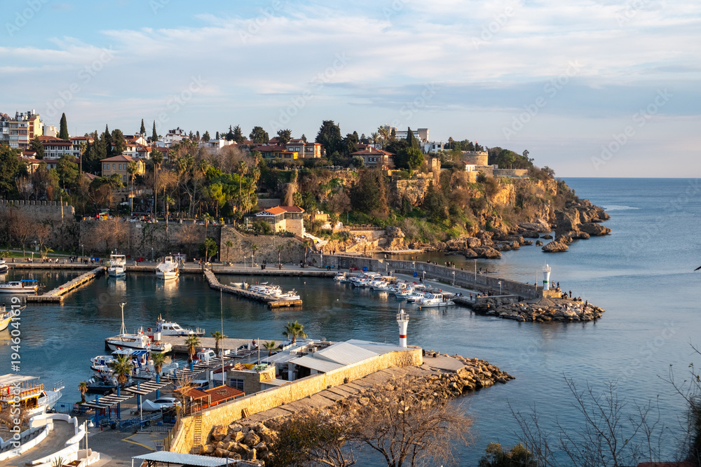 Obraz premium Panoramic view of Kaleici marina and the historic old town of Antalya with boats in the harbor and warm golden hour sunset light illuminating the Mediterranean coastline in southern Türkiye.