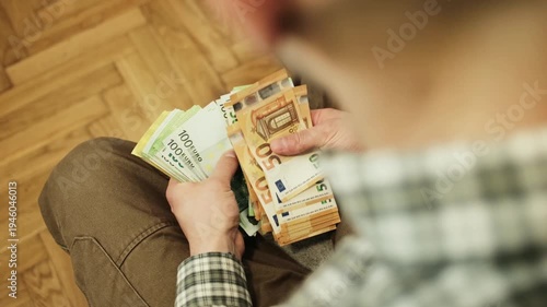 Top view of hands holding and counting a large bundle of euro banknotes while sitting. Concept of personal finance, income management, savings and cash wealth