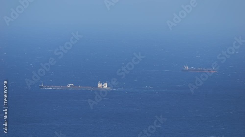 Telephoto view of two cargo vessels travelling across open sea under windy conditions. Maritime transport scene illustrating global shipping routes and ocean logistics.
