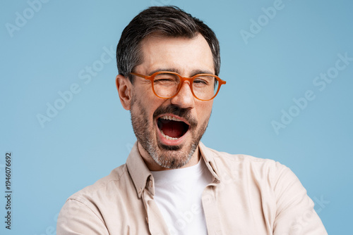 Happy man winking, laughing loudly, wearing orange glasses against a blue background