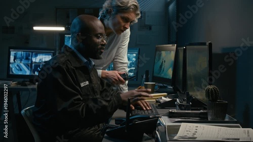 Side view shot of man and woman working together in security control room while watching surveillance footage and pointing at computer monitors during night shift, copy space