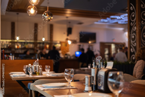 elegant restaurant interior with warm ambient lighting, blurred background, and perfectly set wooden tables with glassware, creating a cozy dining atmosphere