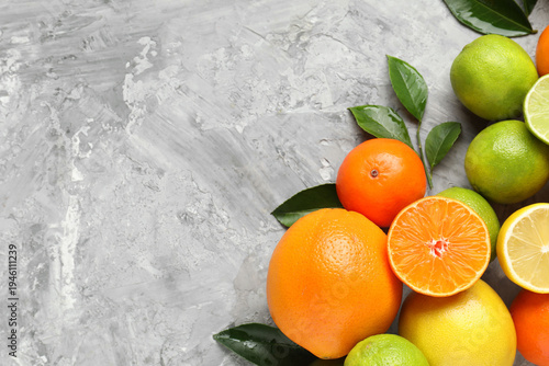 Different fresh citrus fruits and green leaves on grey table, flat lay. Space for text