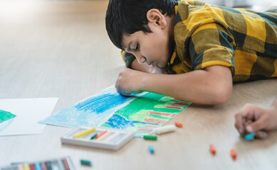 Close up indian arab boy drawing with crayons on the floor during an art activity in a bright classroom setting. Education back to school earth day concept