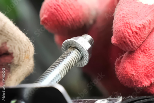 Obraz na plátne Screwing the nut onto the bolt with a hand in a red glove.