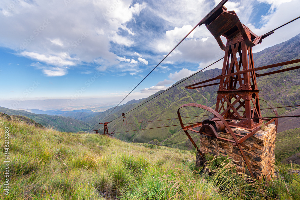 Fototapeta premium Rusty industrial mining structure and cables on a mountain slope overlooking a deep valley, historic mining site.