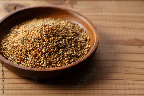 Mixed bird seeds in a wooden bowl on a wooden table