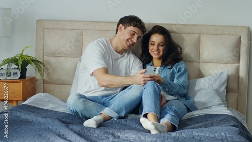 Photos Happy Caucasian couple using smartphone together on bed at home bedroom smiling