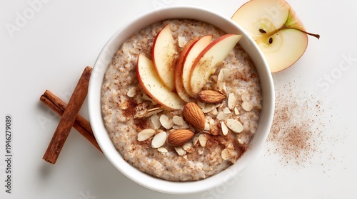 Warm oatmeal bowl with sliced apples, almonds, and cinnamon on white surface