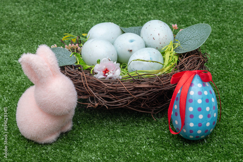 Easter composition with pink bunny, bird's nest and decorated egg on green grass.