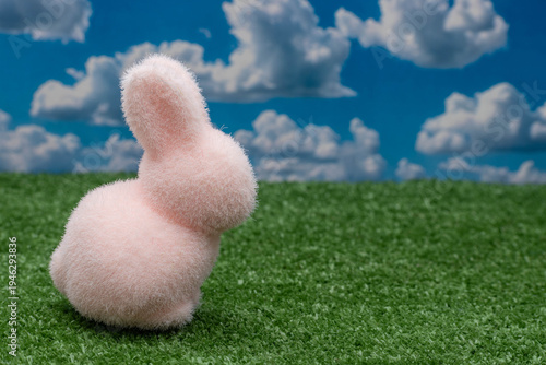 Cute pink fuzzy Easter bunny on green grass with copy space.