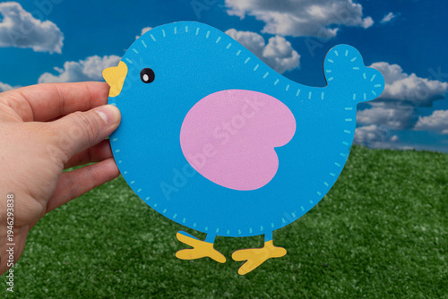 Hand holding a decorative blue bird cutout against a spring background.
