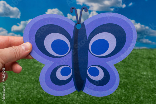Hand holding a decorative purple butterfly against a spring sky.