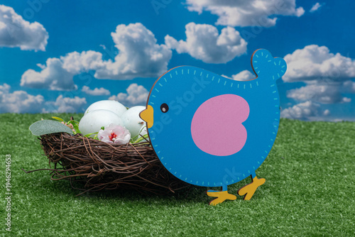 Cute blue bird decoration and nest with speckled eggs on green grass.