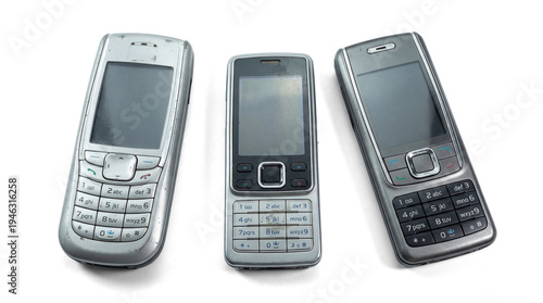 Canvastavla three classic silver mobile phones with physical keypads, viewed from an angle against a transparent background, representing early mobile device technology