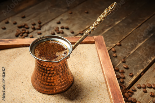 Bild auf Leinwand Cezve of hot Turkish coffee in sand and beans on wooden background