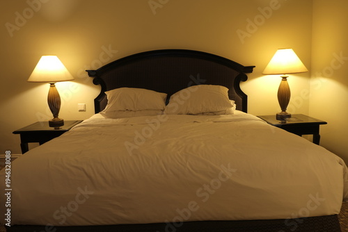 Warmly lit hotel bedroom with neatly made bed, soft pillows and two bedside lamps, inviting restful sleep at night.
