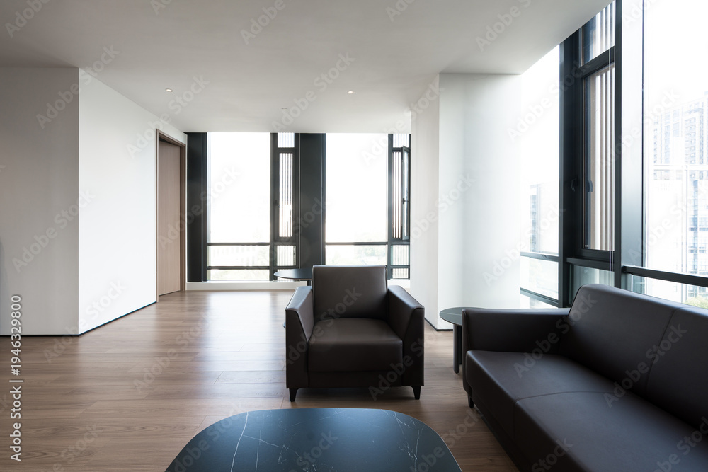 Fototapeta premium Modern minimalist living room with black leather sofa and armchair on wooden flooring near floor-to-ceiling windows