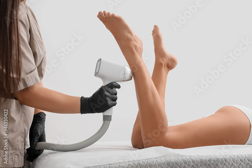 Fotografía Female cosmetologist performing photoepilation on client's legs against white ba