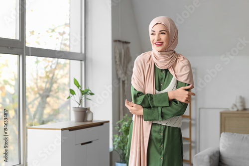 Bild auf Leinwand Beautiful young happy stylish Muslim woman in hijab near window at home