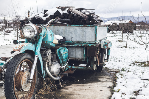An old vintage motorcycle loaded with snow-covered firewood