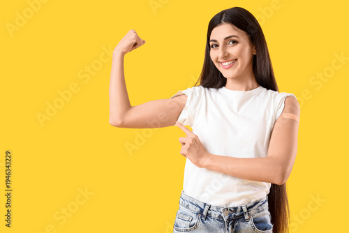 Young woman with medical patch showing muscles after vaccination on yellow ba...