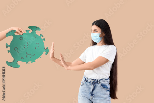 Young woman in medical mask rejecting paper virus on beige background. Immuni...