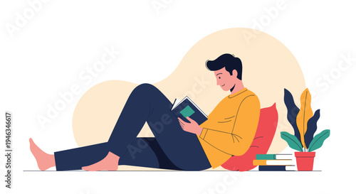 Young man is lying comfortably on the floor and reading a book while leaning against a pillow in his home.