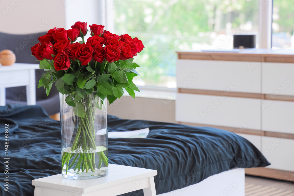 Obraz premium Vase with beautiful red roses on bedside table in stylish bedroom