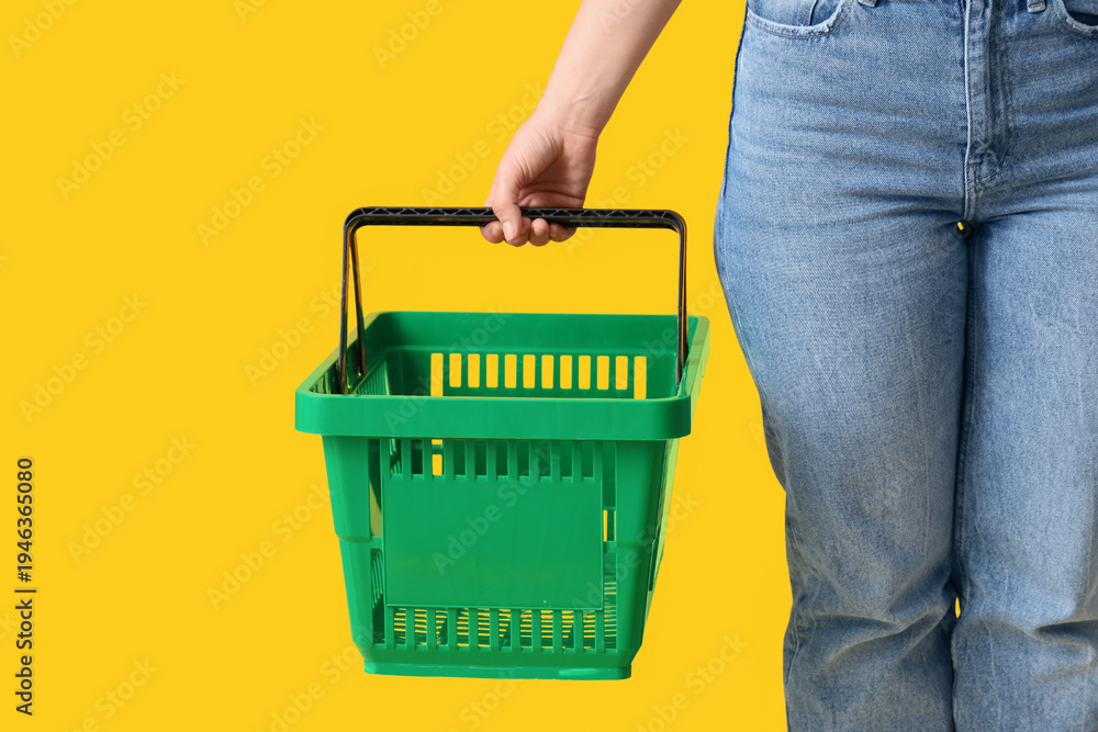 Fototapeta premium Woman with green shopping basket on yellow background