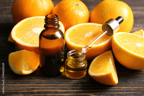 Bottles of orange essential oil and fresh fruits on wooden background