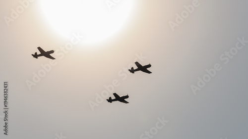 Three planes flying in formation silhouetted against a bright sun and clear sky during an aerial aviation display