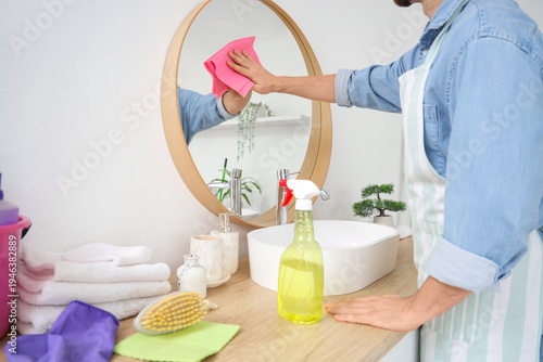 Young man cleaning mirror i...