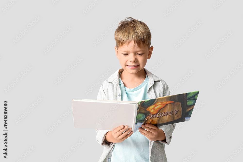 Fototapeta premium Cute little boy reading book on grey background