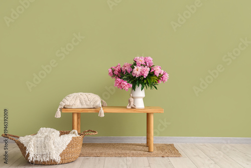 Vase with peonies flowers and pillow on bench in stylish living room