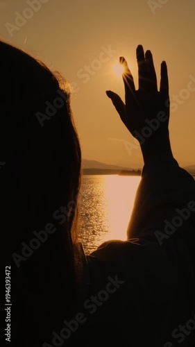 A praying girl stretches out her hand to the sun against the sunset, asking for God's blessing. The concept of aspiration, luck and inspiration. Vertical video.